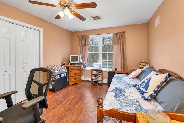 bedroom featuring ceiling fan, wood finished floors, a baseboard radiator, visible vents, and a closet