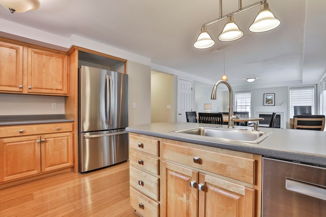 kitchen with dark countertops, a sink, light wood finished floors, decorative light fixtures, and stainless steel appliances