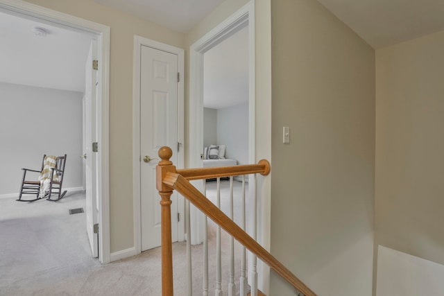hallway featuring baseboards, carpet flooring, and an upstairs landing