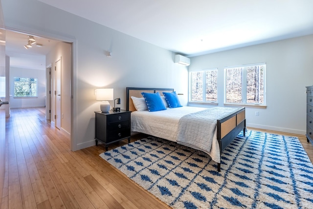 bedroom featuring baseboards, light wood finished floors, and a wall mounted air conditioner