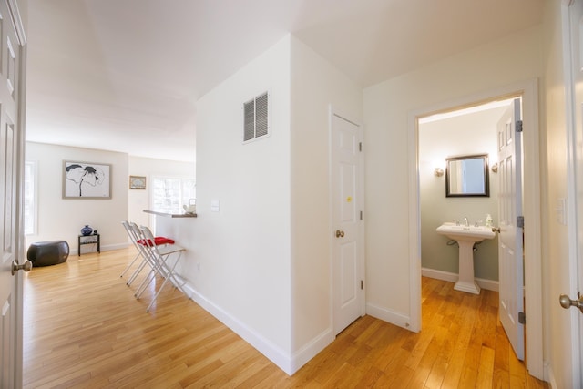corridor featuring baseboards, visible vents, a sink, and light wood finished floors