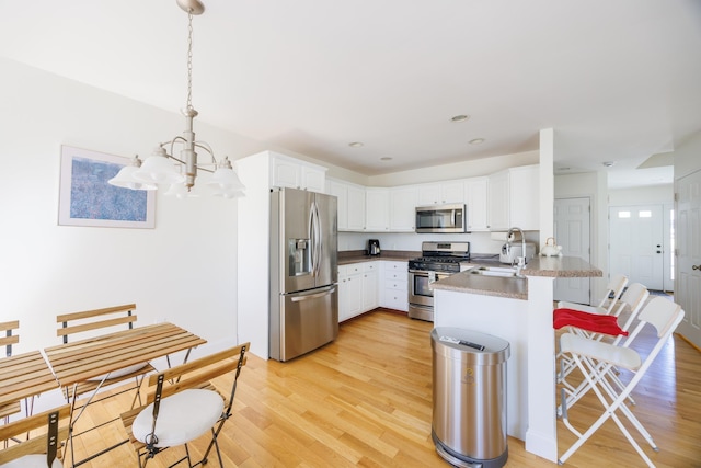 kitchen featuring a peninsula, a kitchen breakfast bar, a sink, appliances with stainless steel finishes, and a notable chandelier