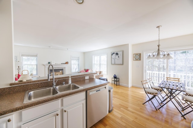 kitchen featuring a fireplace, a sink, white cabinets, open floor plan, and dishwashing machine