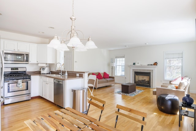 kitchen with appliances with stainless steel finishes, a sink, white cabinets, a peninsula, and light wood-style flooring