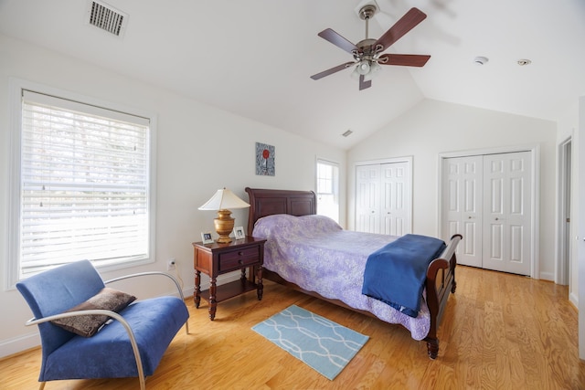 bedroom featuring ceiling fan, visible vents, light wood-style floors, multiple closets, and vaulted ceiling