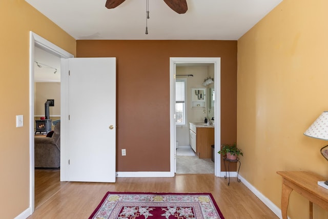 bedroom featuring a wood stove, baseboards, a sink, light wood finished floors, and ensuite bath