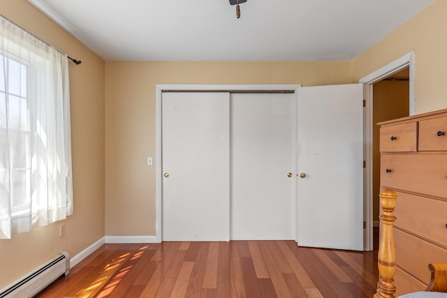 unfurnished bedroom with baseboards, a baseboard radiator, a closet, and wood finished floors