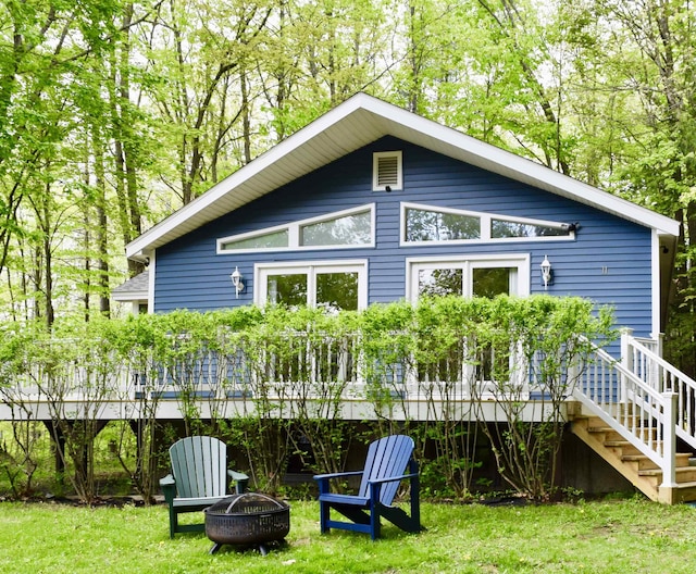 rear view of property with a lawn, a fire pit, a deck, and stairway