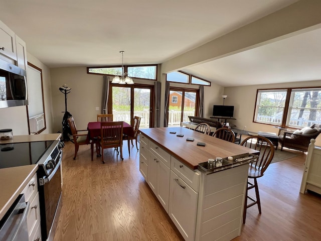 kitchen with wooden counters, a breakfast bar area, lofted ceiling with beams, light wood-style flooring, and appliances with stainless steel finishes