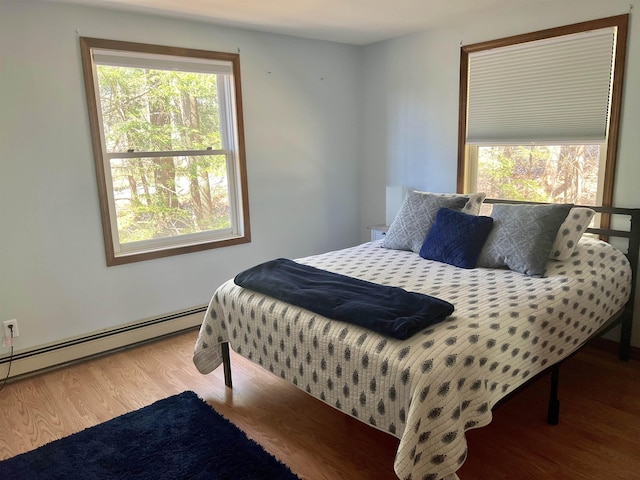 bedroom featuring a baseboard heating unit, wood finished floors, and multiple windows