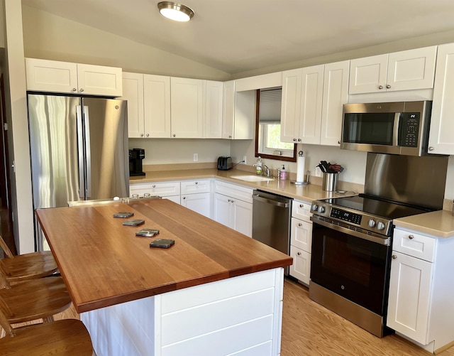 kitchen with butcher block counters, white cabinets, a sink, vaulted ceiling, and stainless steel appliances