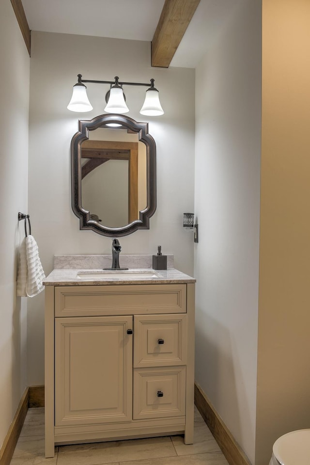 bathroom with beamed ceiling, toilet, baseboards, and vanity
