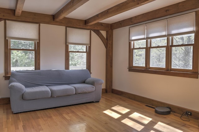 living room featuring baseboards, light wood-type flooring, beam ceiling, and visible vents