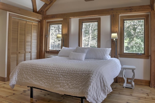 bedroom featuring a closet, baseboards, vaulted ceiling, and light wood finished floors