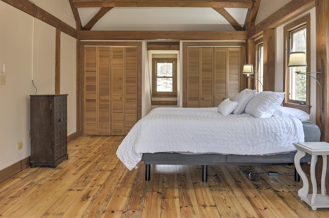 bedroom featuring light wood-style floors, baseboards, two closets, and multiple windows