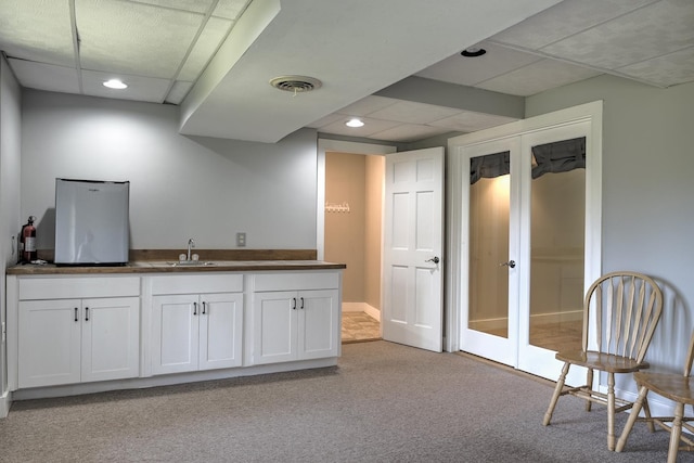 interior space with white cabinets, dark countertops, light colored carpet, a sink, and french doors