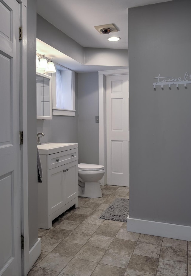 half bathroom with vanity, baseboards, and toilet