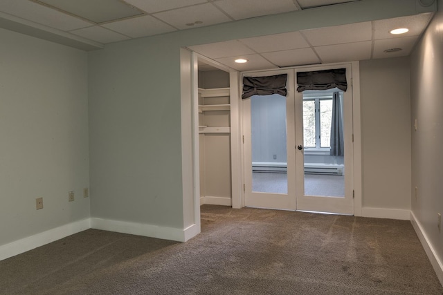 empty room featuring dark colored carpet, a paneled ceiling, a baseboard heating unit, and french doors