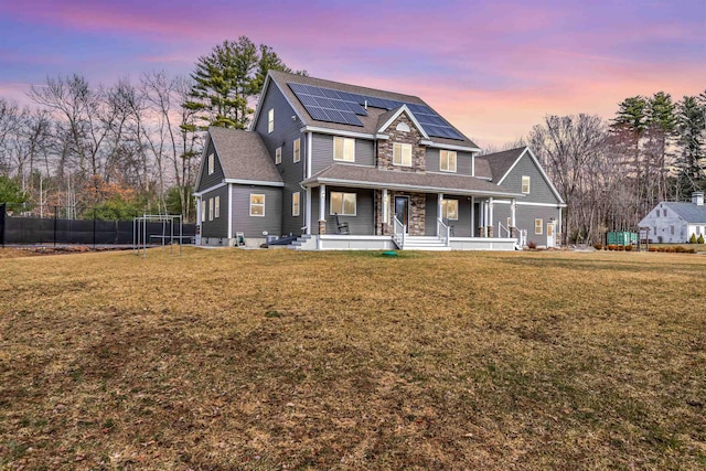 view of front facade with a porch, solar panels, a shingled roof, and a front yard