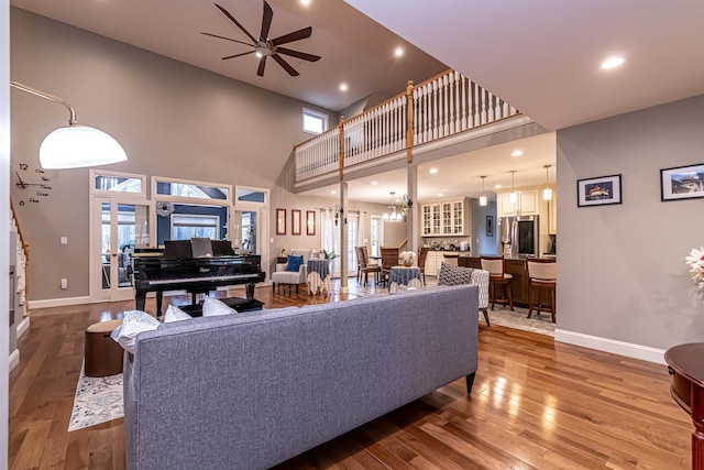 living area featuring baseboards, ceiling fan, a high ceiling, and hardwood / wood-style floors