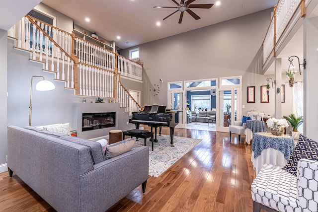 living area with ceiling fan, a high ceiling, stairway, and hardwood / wood-style floors