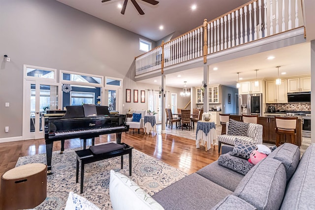 living room with baseboards, hardwood / wood-style flooring, a high ceiling, and ceiling fan with notable chandelier
