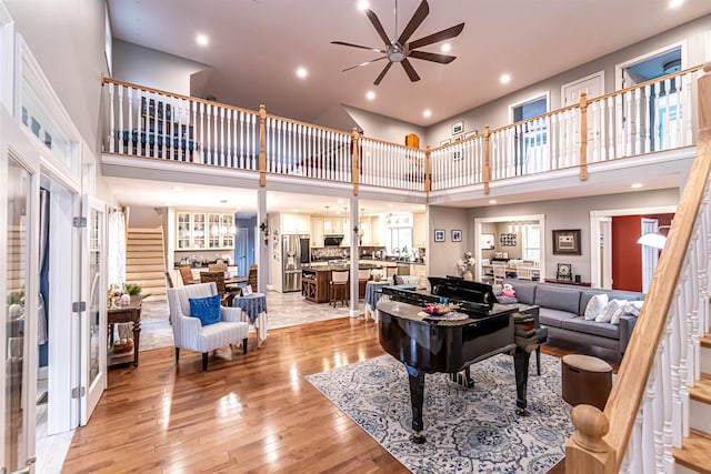 living room with light wood-type flooring, a ceiling fan, stairs, and a high ceiling