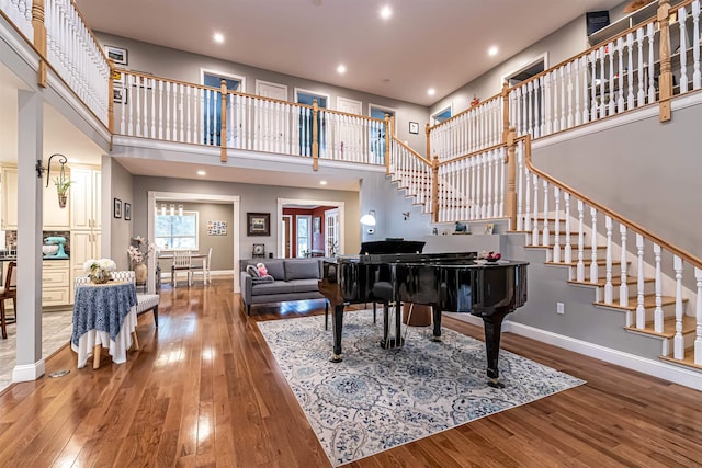 living area with stairs, a towering ceiling, hardwood / wood-style floors, baseboards, and recessed lighting