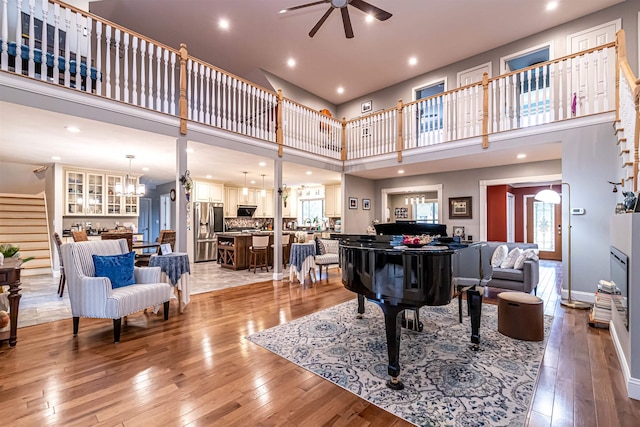 living area featuring recessed lighting, a high ceiling, ceiling fan with notable chandelier, and light wood finished floors