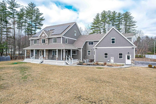 back of house featuring covered porch, a yard, roof mounted solar panels, and roof with shingles