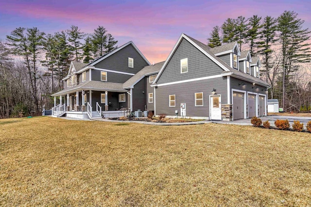 back of property at dusk with a porch, an attached garage, a lawn, and concrete driveway