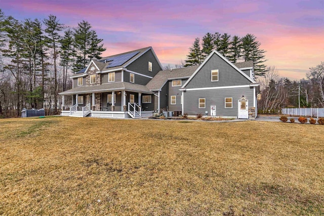 back of house at dusk featuring a lawn, covered porch, and solar panels