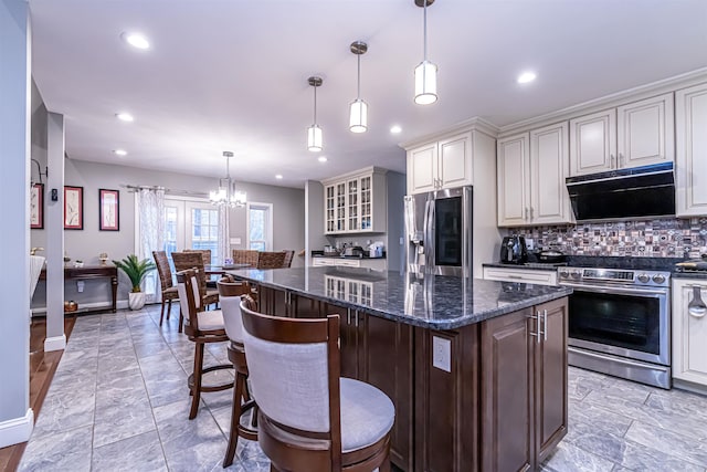 kitchen featuring decorative backsplash, a kitchen island, under cabinet range hood, a chandelier, and appliances with stainless steel finishes