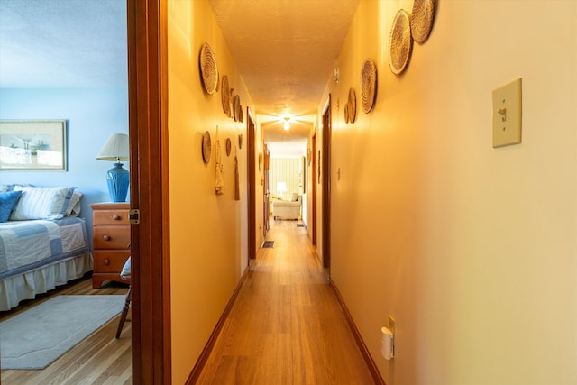 corridor featuring baseboards, a textured ceiling, and light wood finished floors