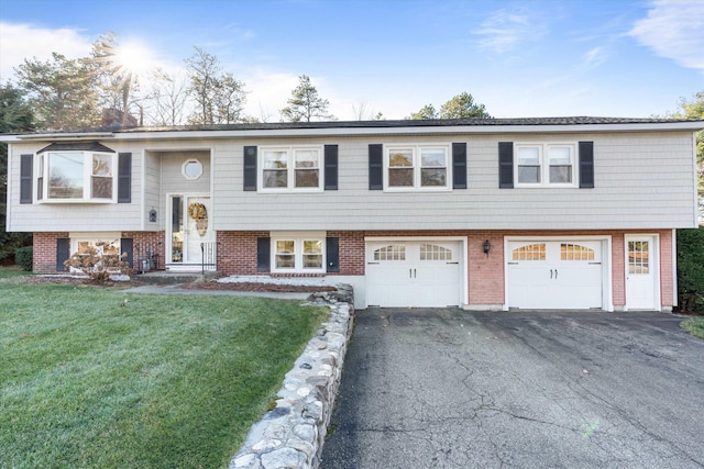 raised ranch with brick siding, an attached garage, a front yard, and aphalt driveway
