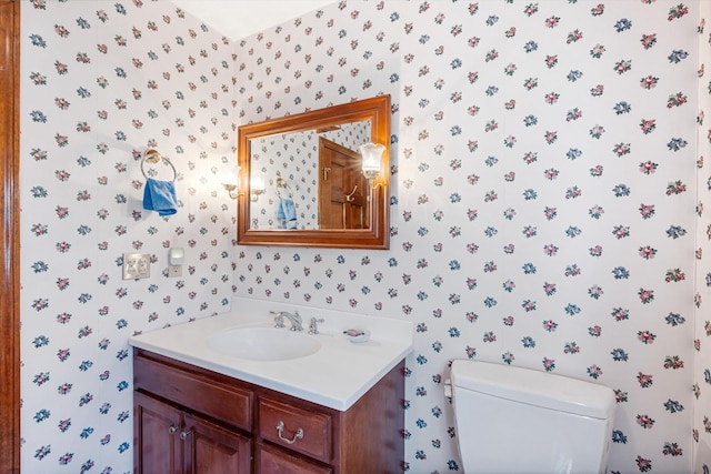 bathroom featuring toilet, wallpapered walls, and vanity