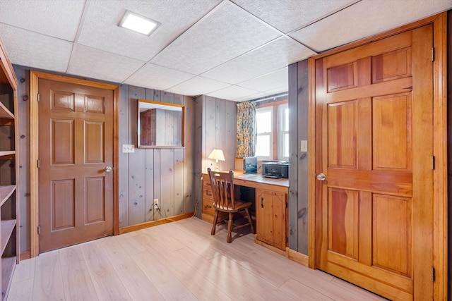office area featuring wooden walls, baseboards, a drop ceiling, and light wood finished floors