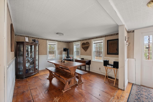 dining area featuring plenty of natural light, a wood stove, a wainscoted wall, and hardwood / wood-style floors