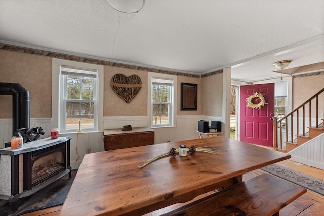 dining area with wood finished floors, a wood stove, stairs, and a wainscoted wall