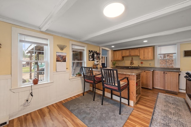 kitchen with wainscoting, a sink, beam ceiling, a peninsula, and light wood-type flooring