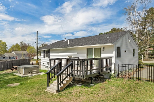 rear view of house featuring roof with shingles, a lawn, a deck, a hot tub, and a fenced backyard