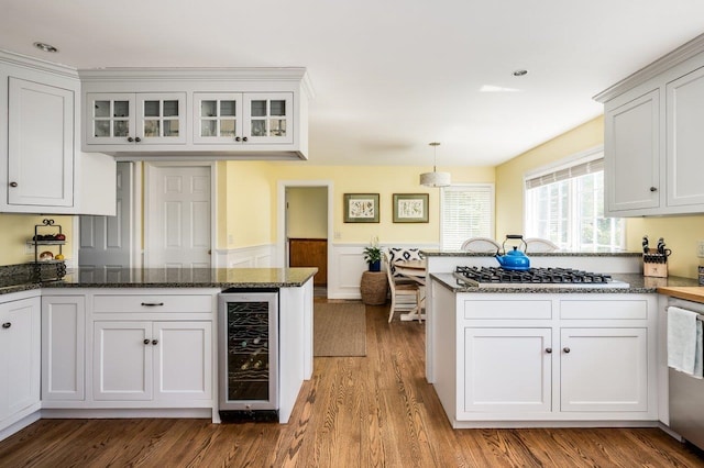 kitchen featuring appliances with stainless steel finishes, wood finished floors, a peninsula, wine cooler, and white cabinetry