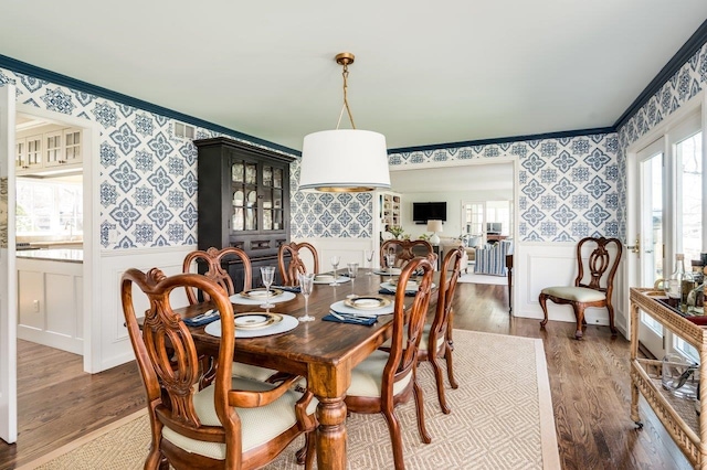 dining area with a wainscoted wall, ornamental molding, wallpapered walls, and wood finished floors