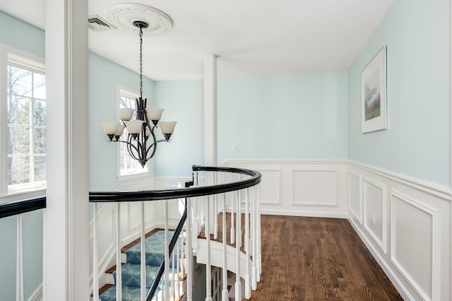 hall featuring an upstairs landing, wainscoting, dark wood-type flooring, and a decorative wall