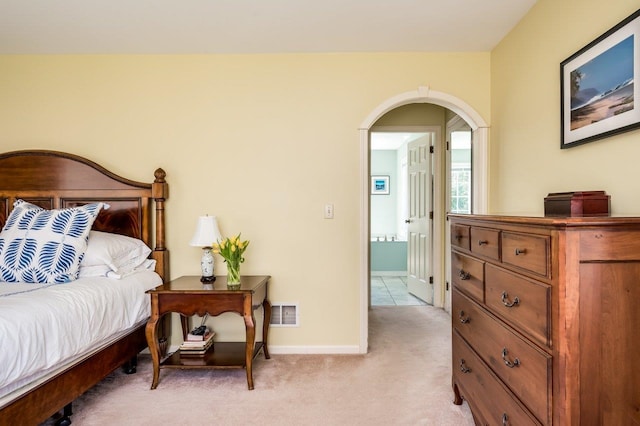 bedroom featuring arched walkways, baseboards, light colored carpet, and visible vents