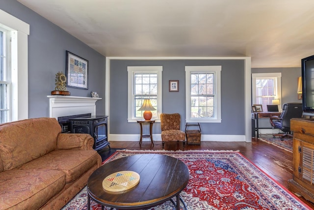 living area featuring dark wood-type flooring, a wood stove, and baseboards