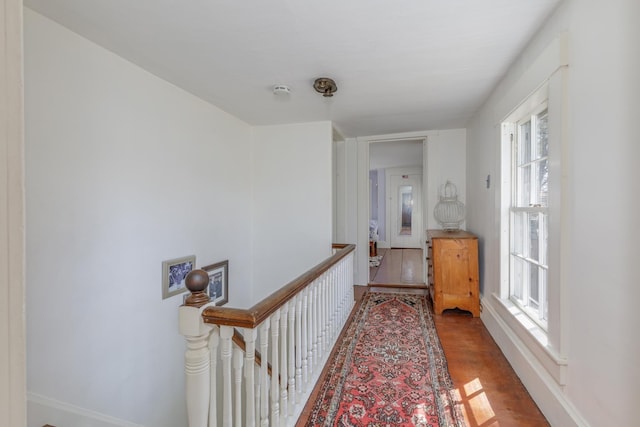 corridor with baseboards, wood finished floors, and an upstairs landing