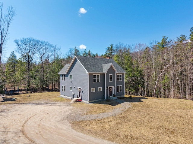view of home's exterior with a forest view, a chimney, a shingled roof, and dirt driveway