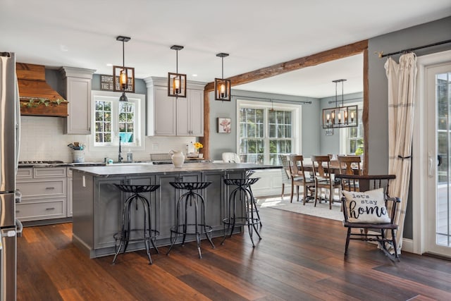 kitchen featuring backsplash, dark wood finished floors, a sink, custom exhaust hood, and a breakfast bar