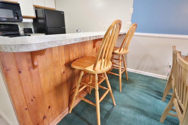 kitchen featuring a breakfast bar area, light countertops, white cabinetry, carpet, and black appliances